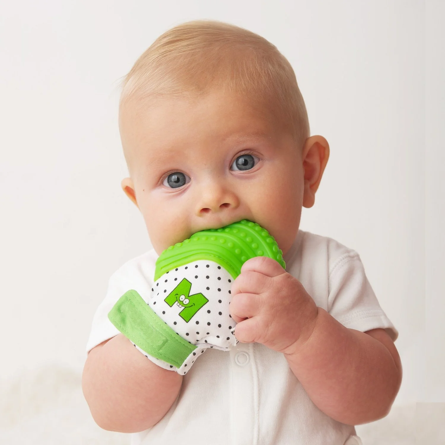 Baby chewing on a colorful teething mitten while playing, combining teething relief with sensory stimulation.